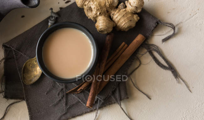 Чашка чая с молоком, корицей, имбирем и кардамоном на бежевой поверхности — стоковое фото