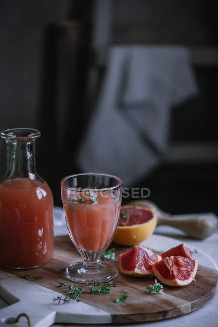 Zumo de pomelo fresco en vidrio y botella con ingrediente en la mesa de la cocina - foto de stock