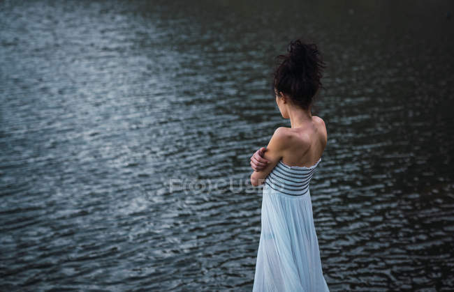 Jovem mulher de vestido branco em pé sozinho na costa do lago — Fotografia de Stock