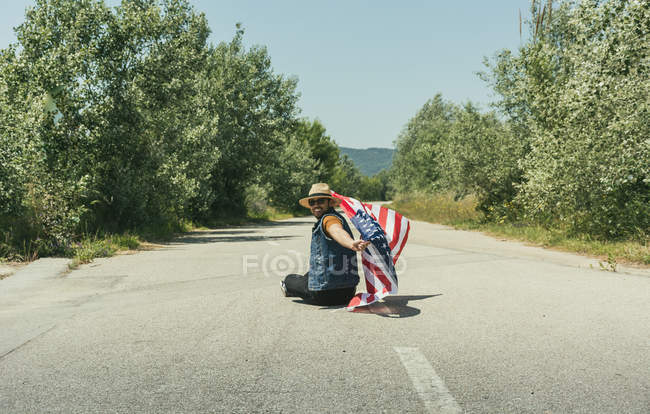 Uomo con bandiera americana seduto su strada — Foto stock