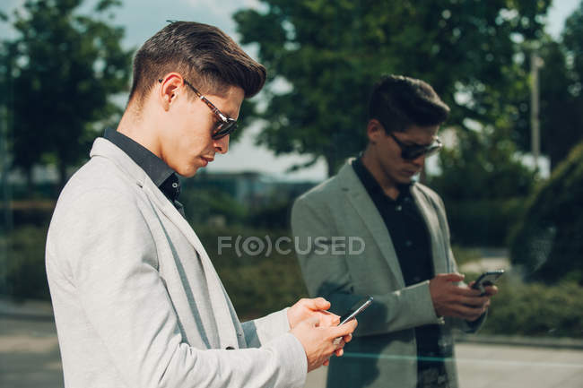 Молодий бізнесмен використовує смартфон біля скляної стіни — стокове фото