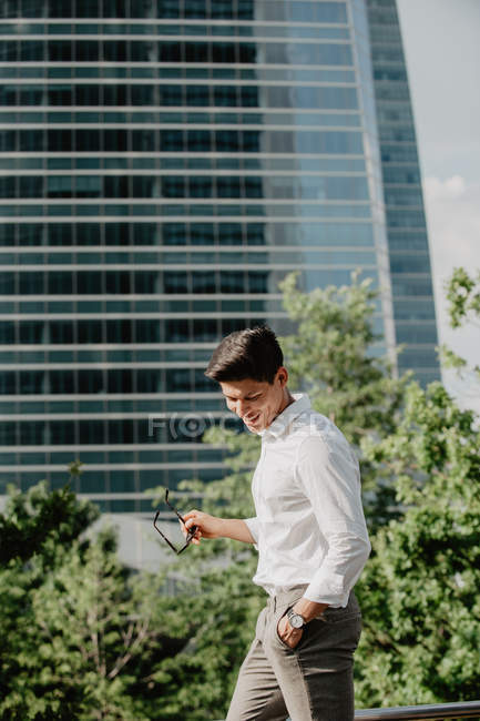 Ridendo giovane uomo d'affari in piedi contro edificio moderno e guardando oltre le spalle — Foto stock