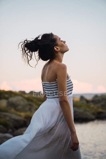 Young brunette standing alone with eyes closed on lake shore — Stock Photo