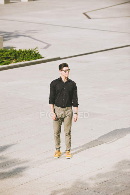 Уверенный в себе человек в черной рубашке и солнцезащитных очках стоит на улице — стоковое фото