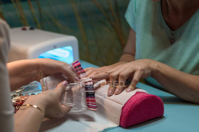 Manicura femenina mostrando paleta de esmalte de uñas al cliente en salón de belleza - foto de stock