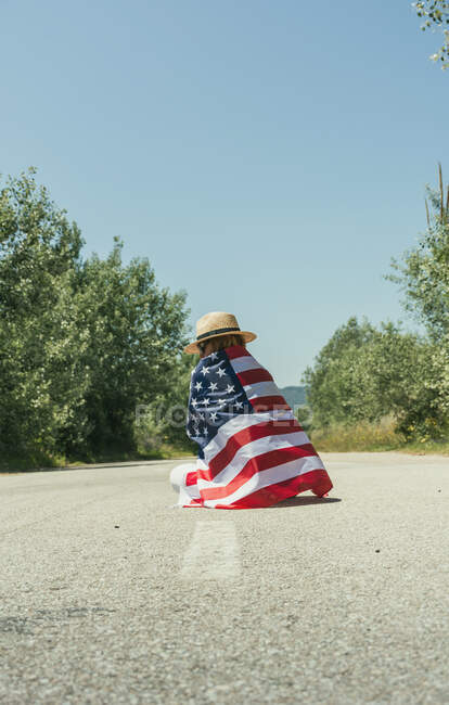 Homme heureux et sautant de joie avec un drapeau américain sur une route solitaire — Photo de stock