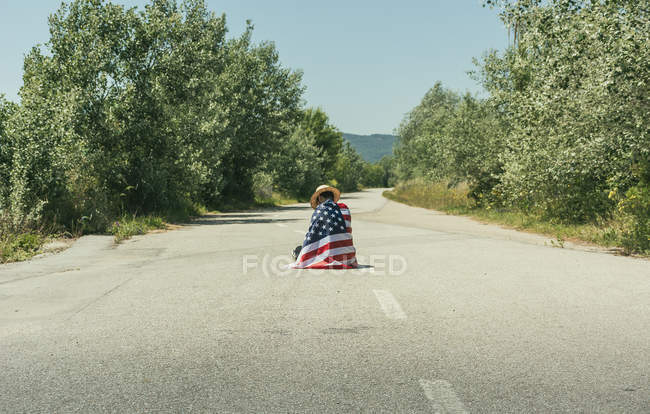 Homme avec drapeau américain assis sur la route — Photo de stock