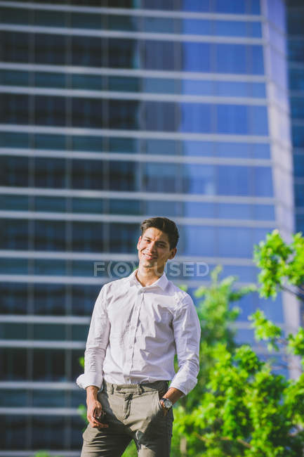 Positivo giovane uomo d'affari in piedi contro edificio moderno e guardando la fotocamera — Foto stock