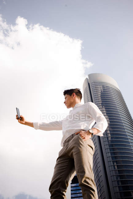 Молодий бізнесмен фотографує зі смартфоном перед будівлею сучасної вежі — стокове фото