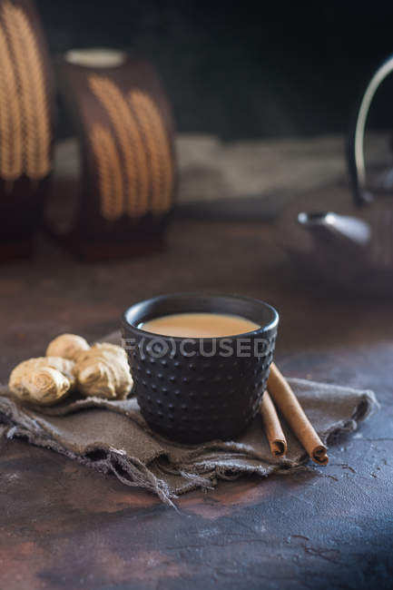 Orientalische Tasse Tee Chai mit Milch mit Zimt auf grauem Tuch auf dunklem Hintergrund — Stockfoto