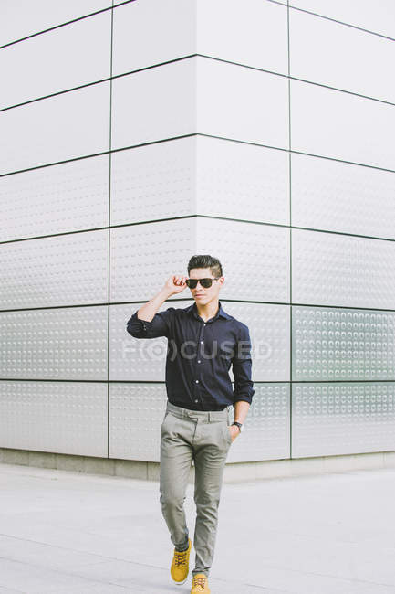 Casual man walking in front of modern building and looking away — Stock Photo