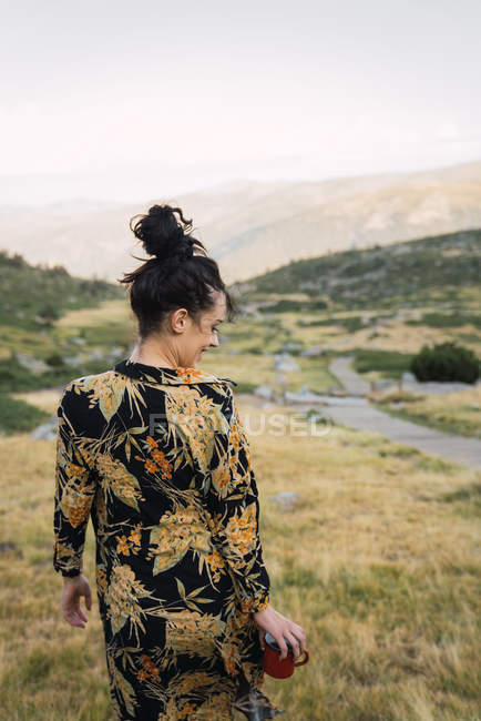 Donna casual in camicia colorata che cammina con la tazza in mano nella valle delle montagne — Foto stock