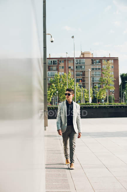 Fiducioso uomo elegante in occhiali da sole a piedi in città — Foto stock