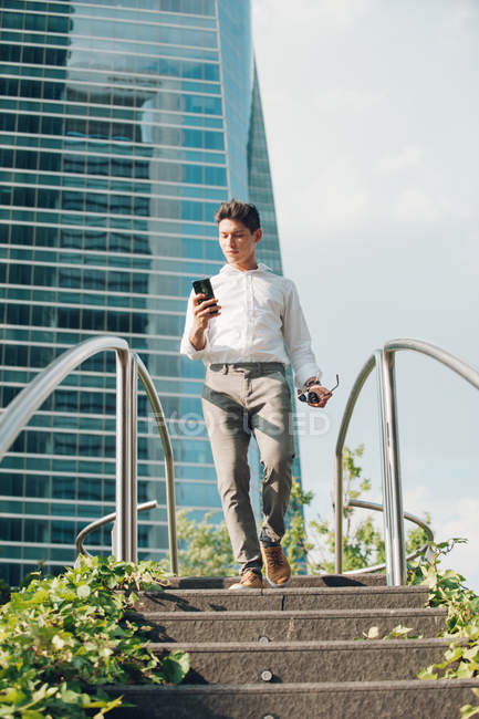 Elegant man with smartphone walking down steps in modern city — Stock Photo