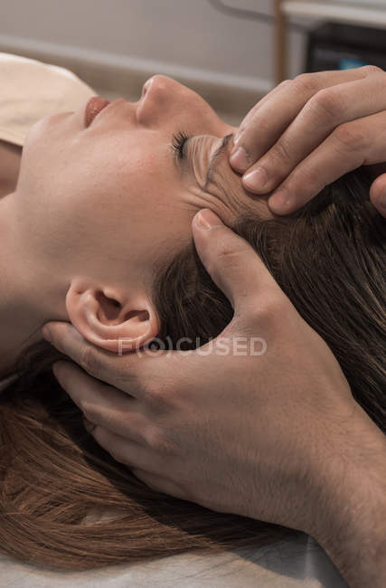 Primer plano del terapeuta masajeando la cara femenina en la sala de masajes - foto de stock