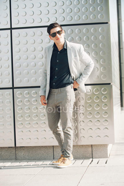 Молодий хлопець в елегантному вбранні стоїть біля стіни будівлі і дивиться на камеру — стокове фото