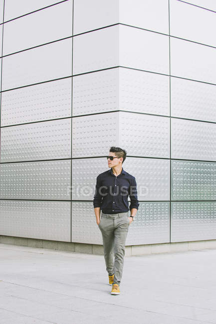 Homem casual andando na frente do edifício moderno e olhando para longe — Fotografia de Stock
