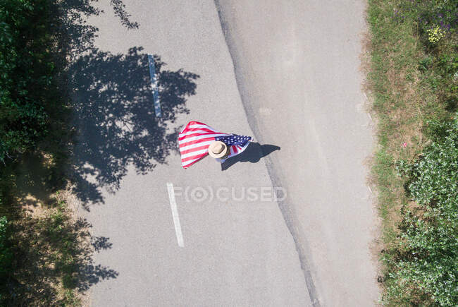 Жінка в капелюсі йде з американським прапором на одинокій дорозі. Спеціальний день для святкування 4 липня. — стокове фото