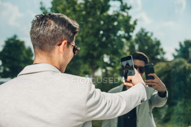 Elegante giovane uomo d'affari che prende selfie con smartphone vicino alla parete di vetro — Foto stock