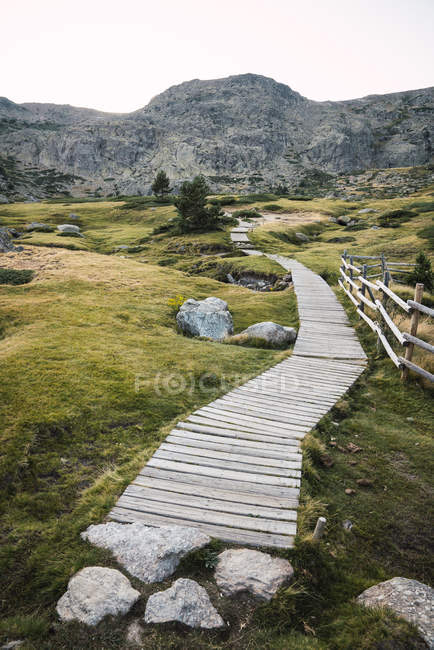 Vista prospectiva da passarela de madeira em terreno verde rochoso com montanhas no fundo, Espanha — Fotografia de Stock