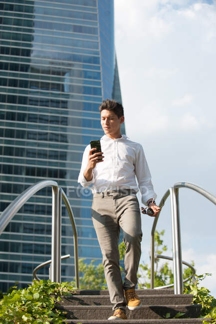 Homem elegante com smartphone descendo degraus na cidade moderna — Fotografia de Stock