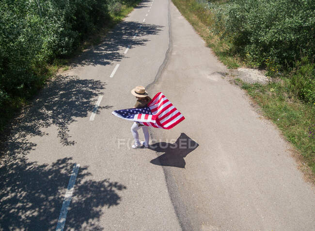 Eine Frau mit Hut geht mit der amerikanischen Flagge auf einer einsamen Straße. Besonderer Tag zur Feier des 4. Juli — Stockfoto