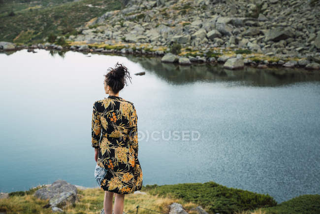 Mulher em rochas de pequeno lago em montanhas, vista traseira — Fotografia de Stock
