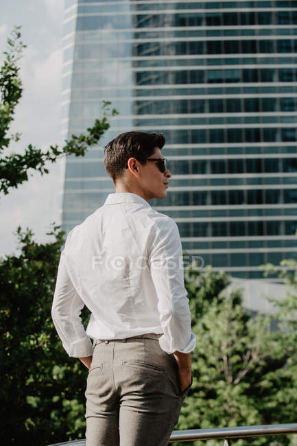 Jeune homme d'affaires en lunettes de soleil debout devant un bâtiment moderne — Photo de stock