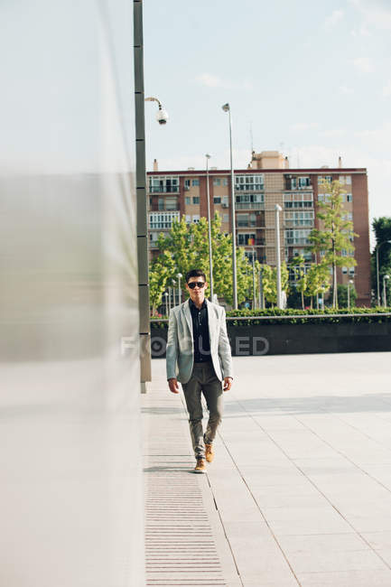 Homem elegante confiante em óculos de sol andando na cidade — Fotografia de Stock