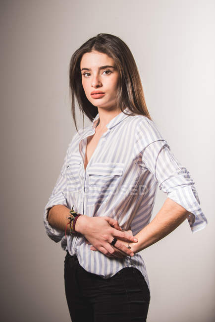 Mujer joven con camisa a rayas posando sobre fondo gris - foto de stock