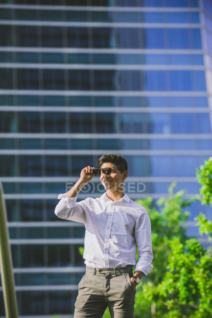 Positive young businessman standing against modern skyscraper — Stock Photo