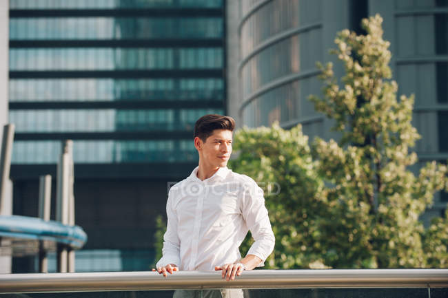 Sorridente jovem empresário em pé perto de trilhos contra arranha-céus modernos — Fotografia de Stock