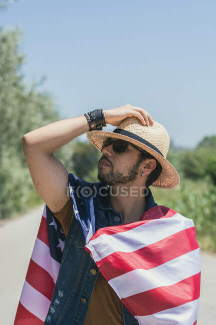 Uomo felice e che salta per la gioia con una bandiera americana su una strada solitaria — Foto stock