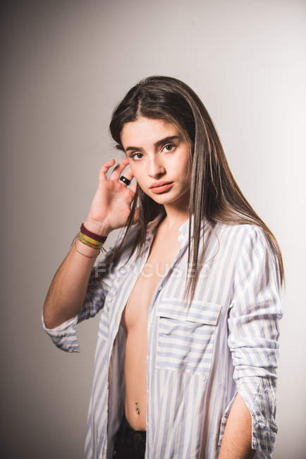 Chica sensual en camisa desabotonada a rayas posando sobre fondo gris - foto de stock