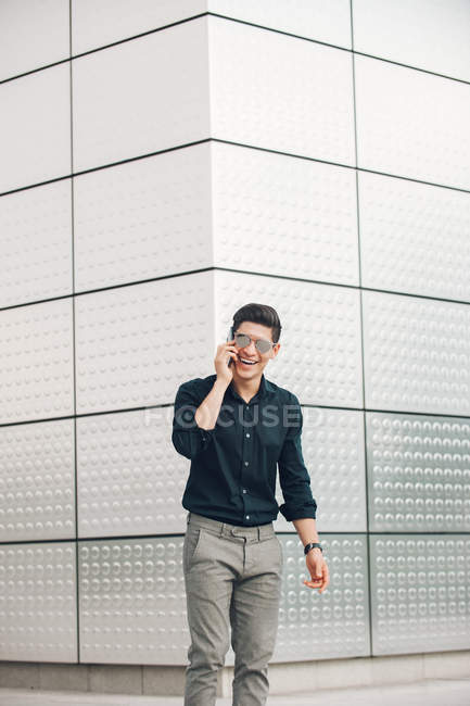 Веселый молодой бизнесмен говорит по телефону против стены здания — стоковое фото