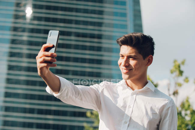 Giovane uomo d'affari scattare selfie con smartphone contro edificio moderno — Foto stock