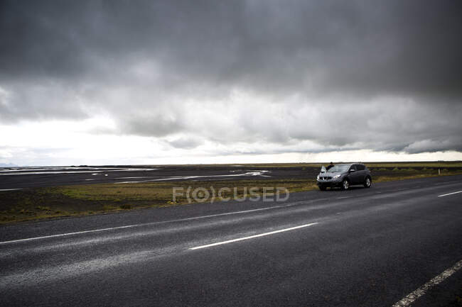 Person near car standing on highway passing between wild land near water in cloudy weather in Iclenad — Stock Photo