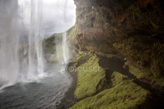 Salpicaduras de cascada de acantilados rocosos verdes, Islandia - foto de stock