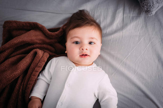 Portrait de bébé garçon curieux couché sur le lit — Photo de stock