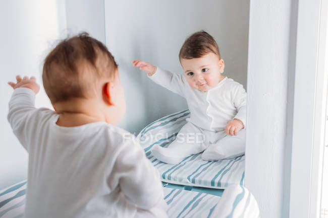 Asombrado dulce bebé chico mirando espejo en vivero - foto de stock