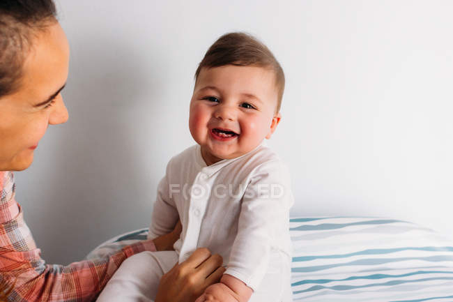 Mère souriante tenant bébé drôle dans la crèche — Photo de stock