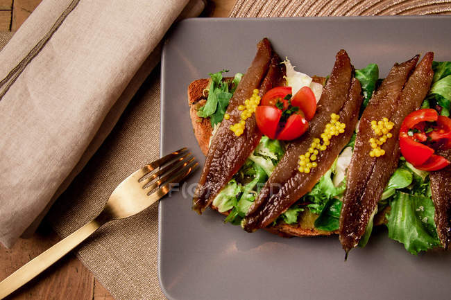 Sandwich with vegetables and fish on grey plate with fork — Stock Photo