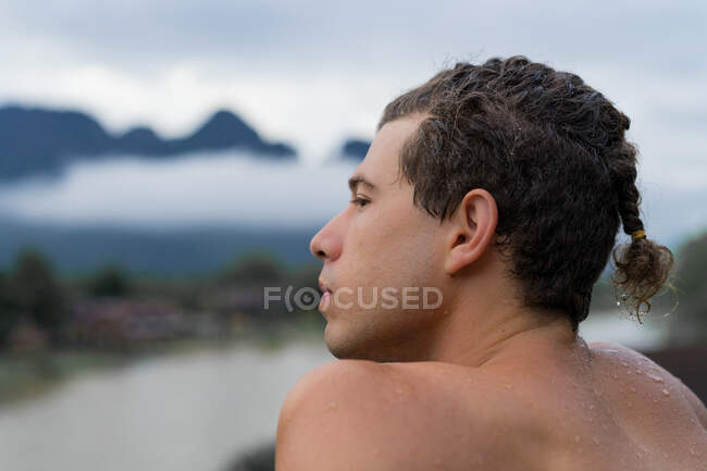 Вид збоку вдумливого чоловіка, що сидить біля річки в природі на розмитому тлі . — стокове фото