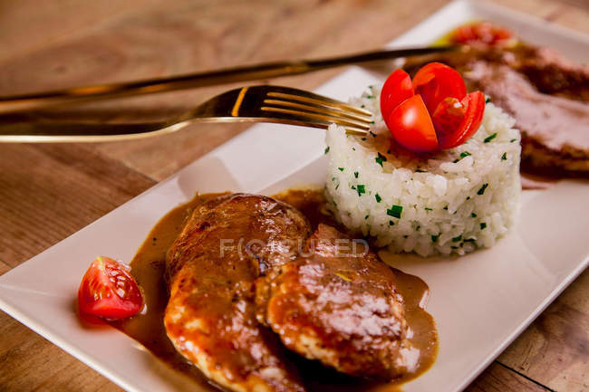 Roasted meat with sauce and rice on white platter with fork and knife — Stock Photo