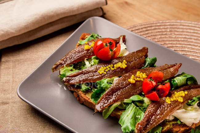 Сендвіч з овочами та рибою на сірій тарілці на килимку — стокове фото