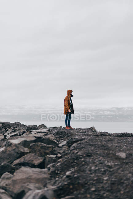 Anonyme Person im Mantel steht an der Küste von grauen Felsen mit nebligem Wasser im Hintergrund, Island. — Stockfoto