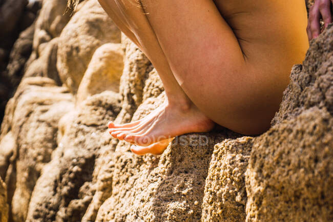 Side view of crop nude woman sitting on rock in sunny day. — Stock Photo
