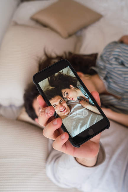 Cheerful young couple taking selfie with smartphone on bed — Stock Photo