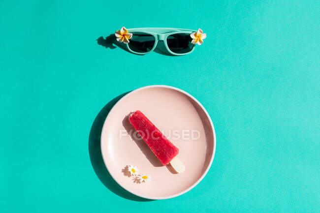 Vista de cima de sorvete rosa em placa branca e óculos de sol em fundo azul — Fotografia de Stock