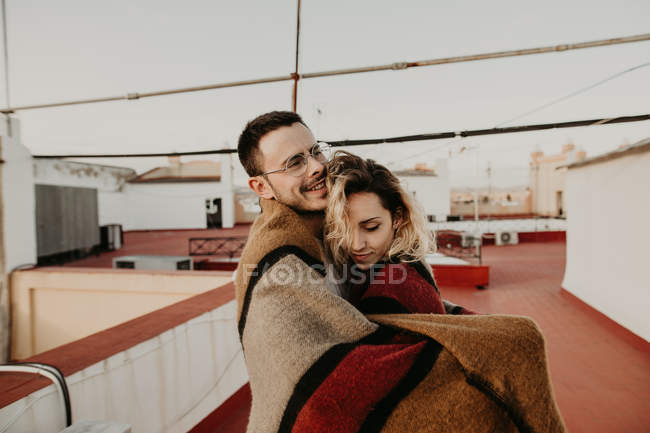 Pareja abrazándose con manta en una terraza - foto de stock
